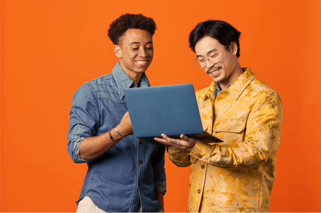 Orange background with two men smiling at computer together